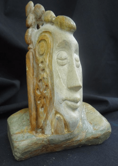 Soapstone Sculpture of smiling man with decoranted headress on stone by artist Hollis Richardson